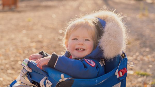 Elias Beals in a backpack carrier, bathed in sunlight, with a joyful expression.​