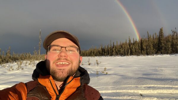 Hunter Keefe Iditarod Musher at Turning Heads Kennel with a Rainbow Behind him