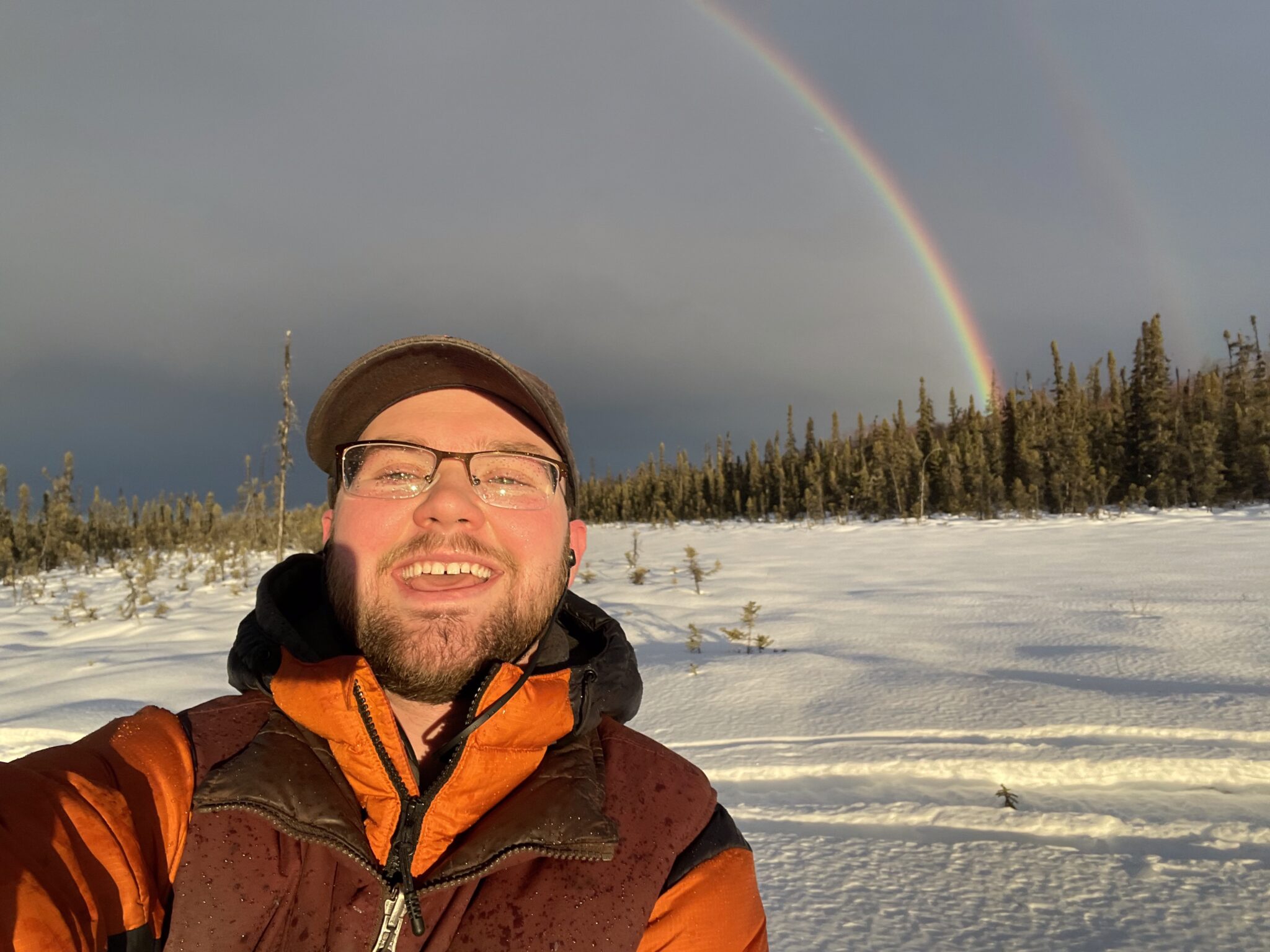 Hunter Keefe Iditarod Musher at Turning Heads Kennel with a Rainbow Behind him